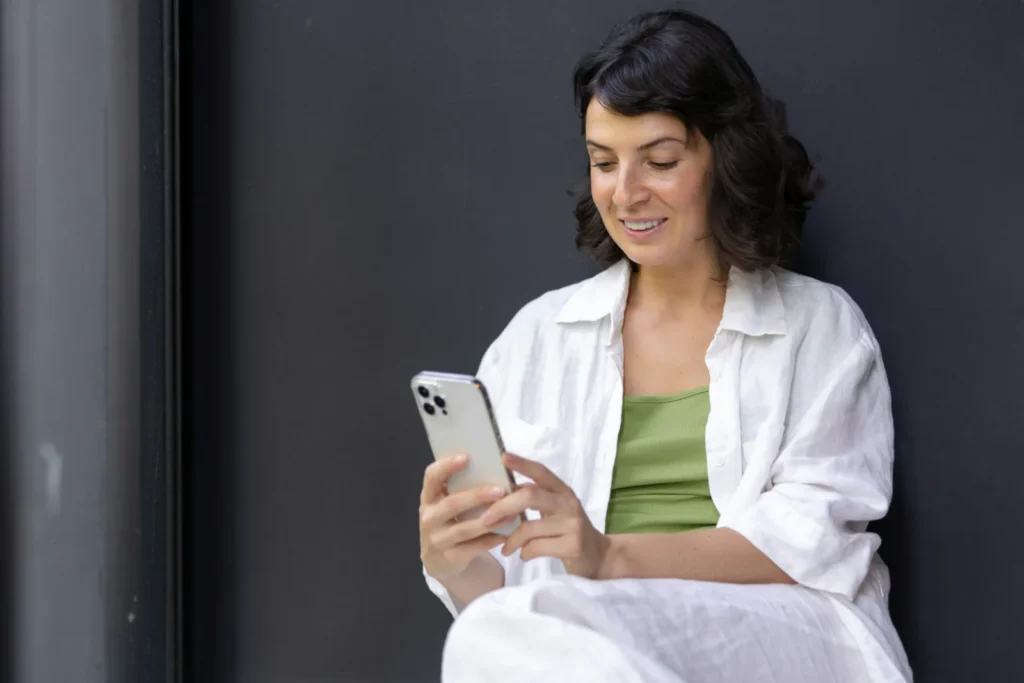 Frau sitzt entspannt und blickt lächelnd auf ihr Smartphone