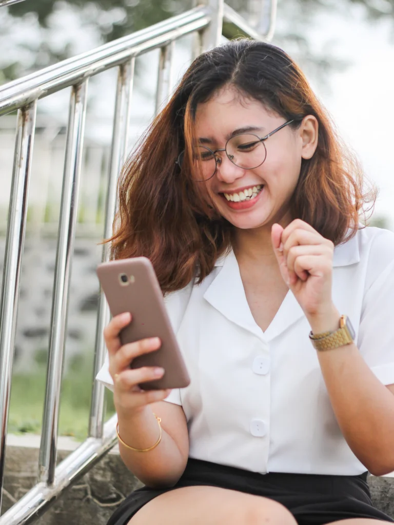 Junge Frau mit Brille lacht beim Blick auf ihr Smartphone